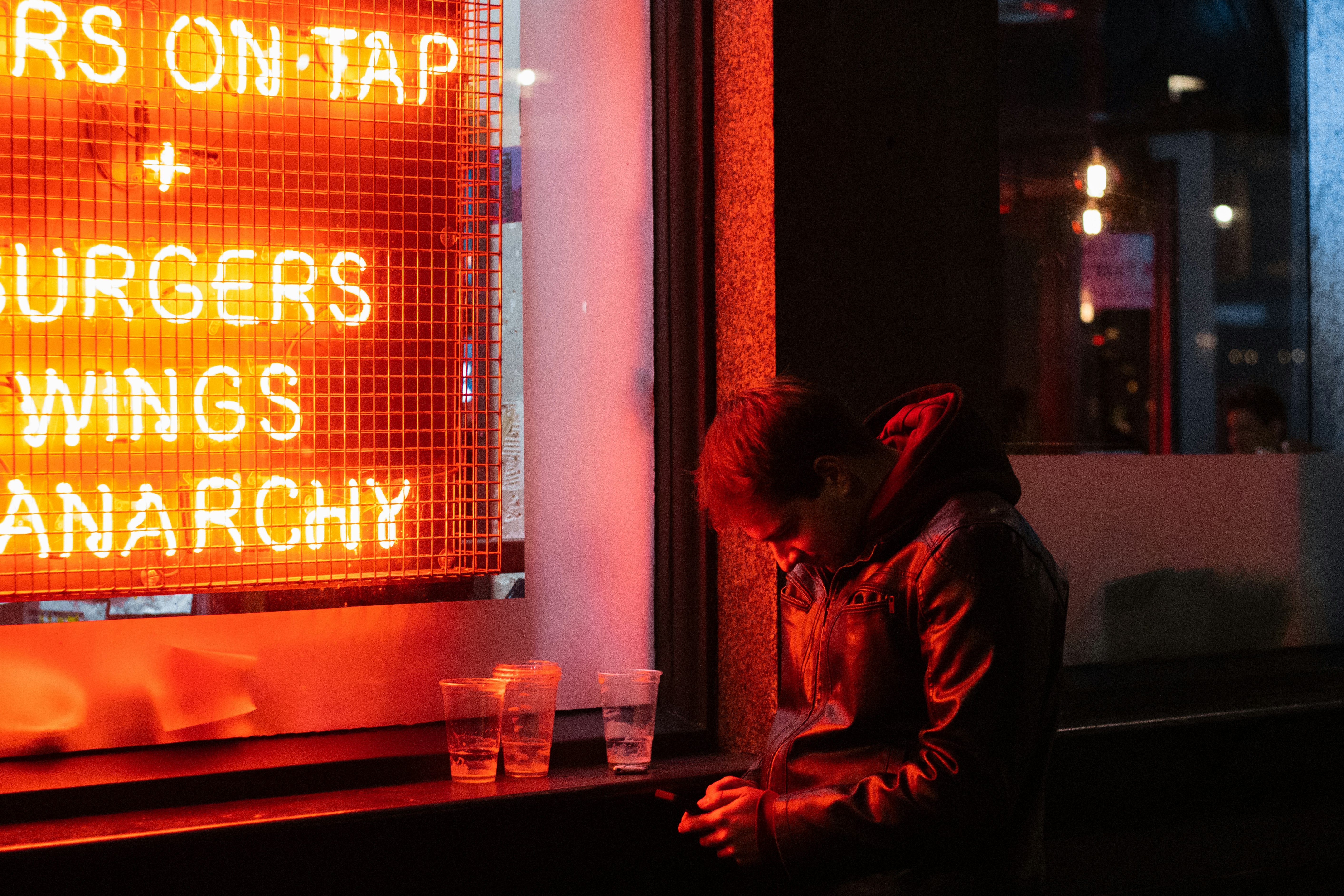 man in black leather jacket sitting beside red and black neon signage